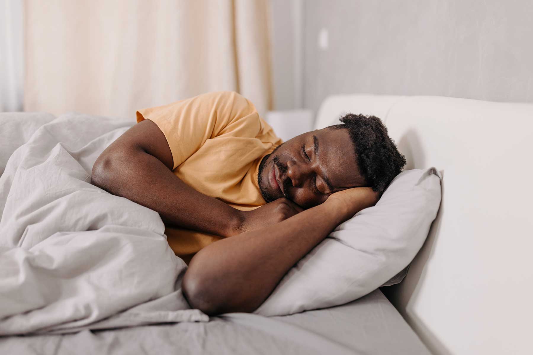 Man peacefully sleeping in bed, lying on his side with a relaxed expression.